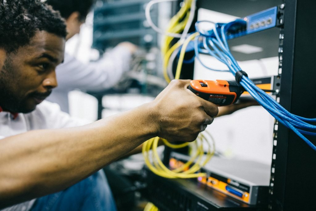 An engineer inspects network cables and connections in a server room, focusing with precision.