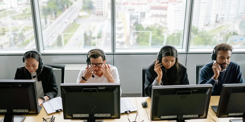 Group of diverse call center employees working at computers in a modern office setting.